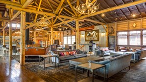 A spacious lodge interior with wooden beams, a grand fireplace, and a variety of seating arrangements. - Grand Lake Lodge (Grand Lake)