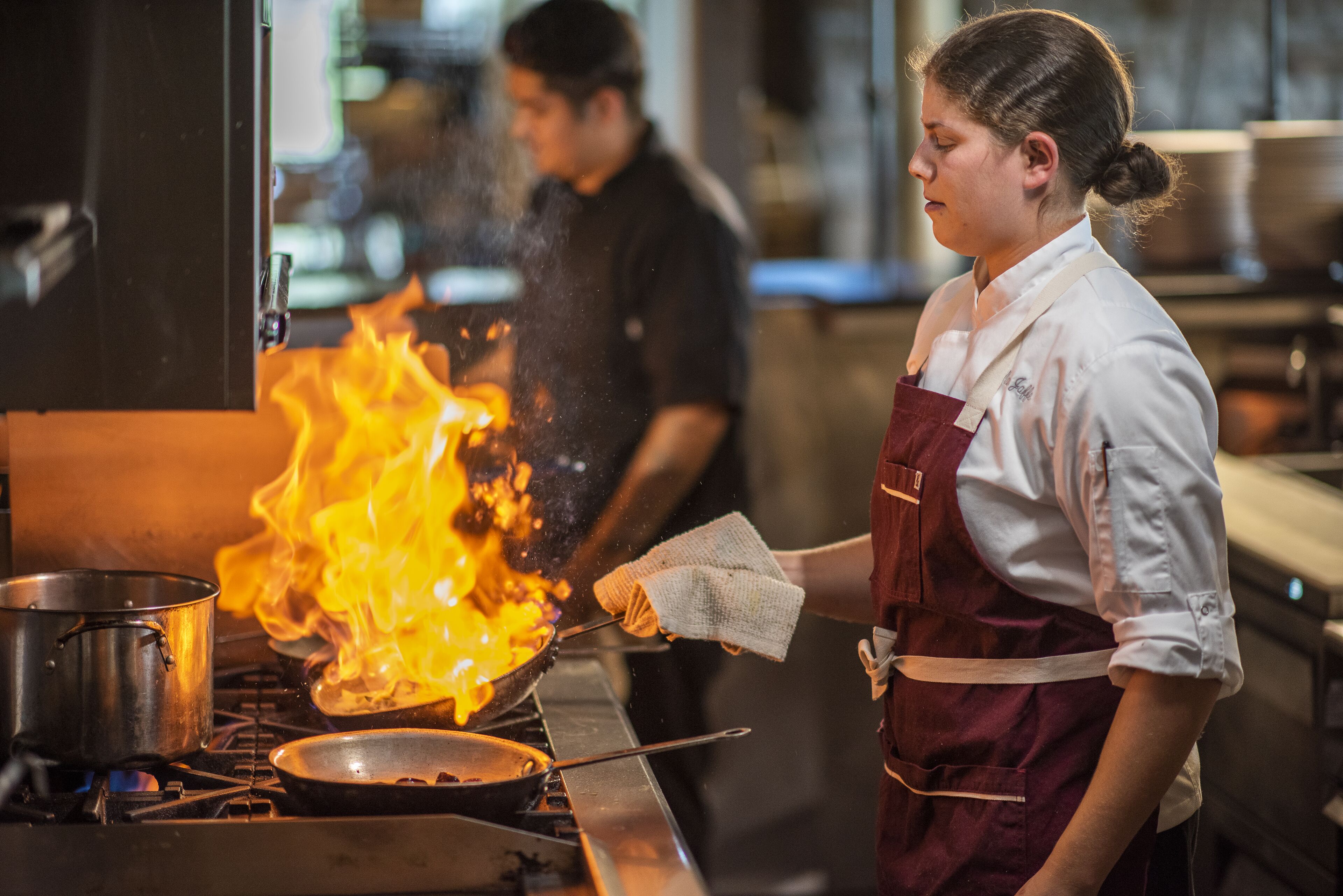 A chef cooking with a pan on a stove with flames.