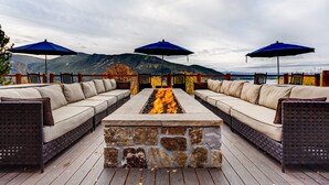 An outdoor seating area with a stone fire feature, three blue umbrellas, and a view of mountains. - Grand Lake Lodge (Grand Lake)