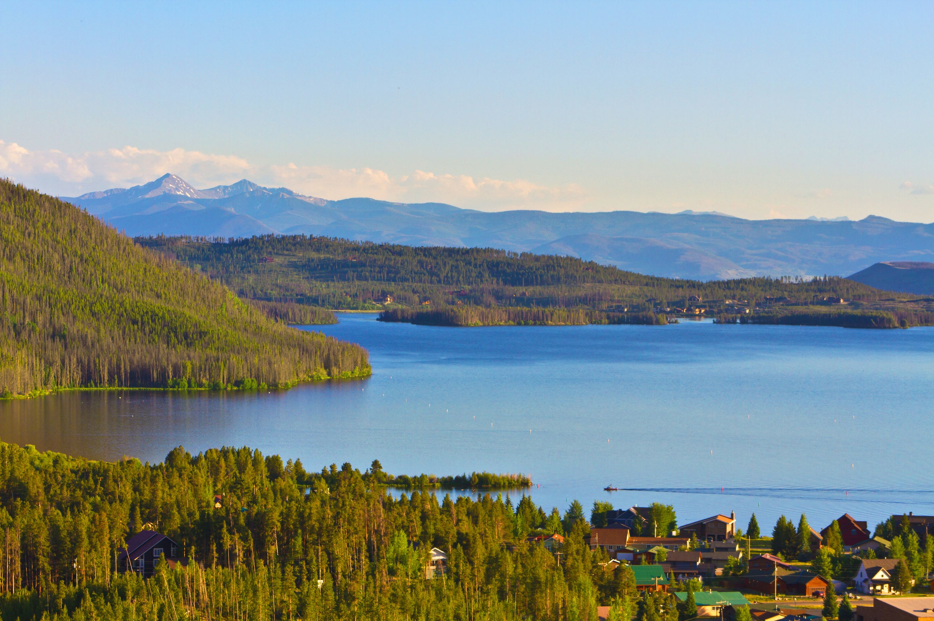 Une vue sur le lac, avec une zone boisée et un petit village composé de maisons et d’immeubles.