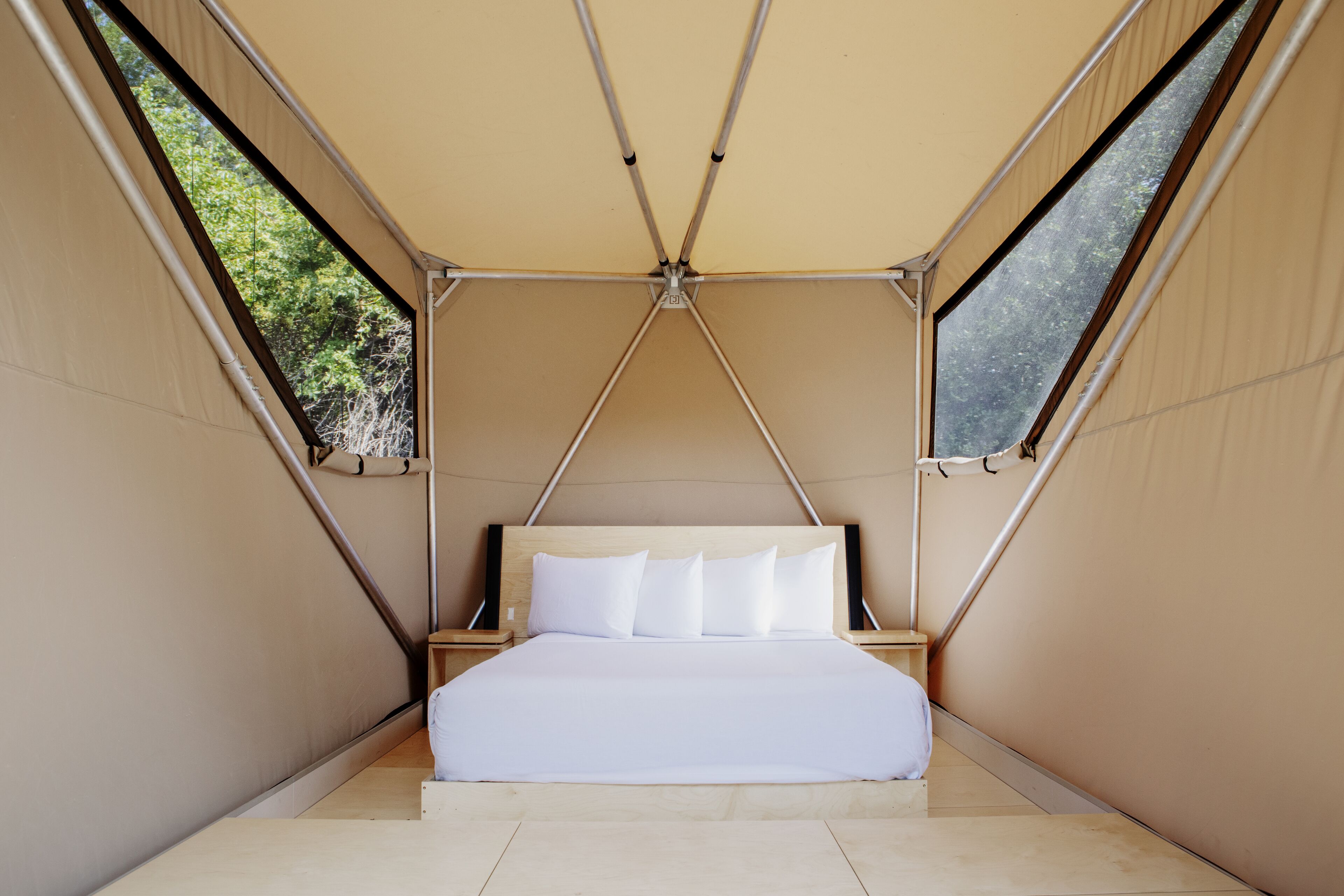 A tented room with a bed, wooden headboard, and two windows.