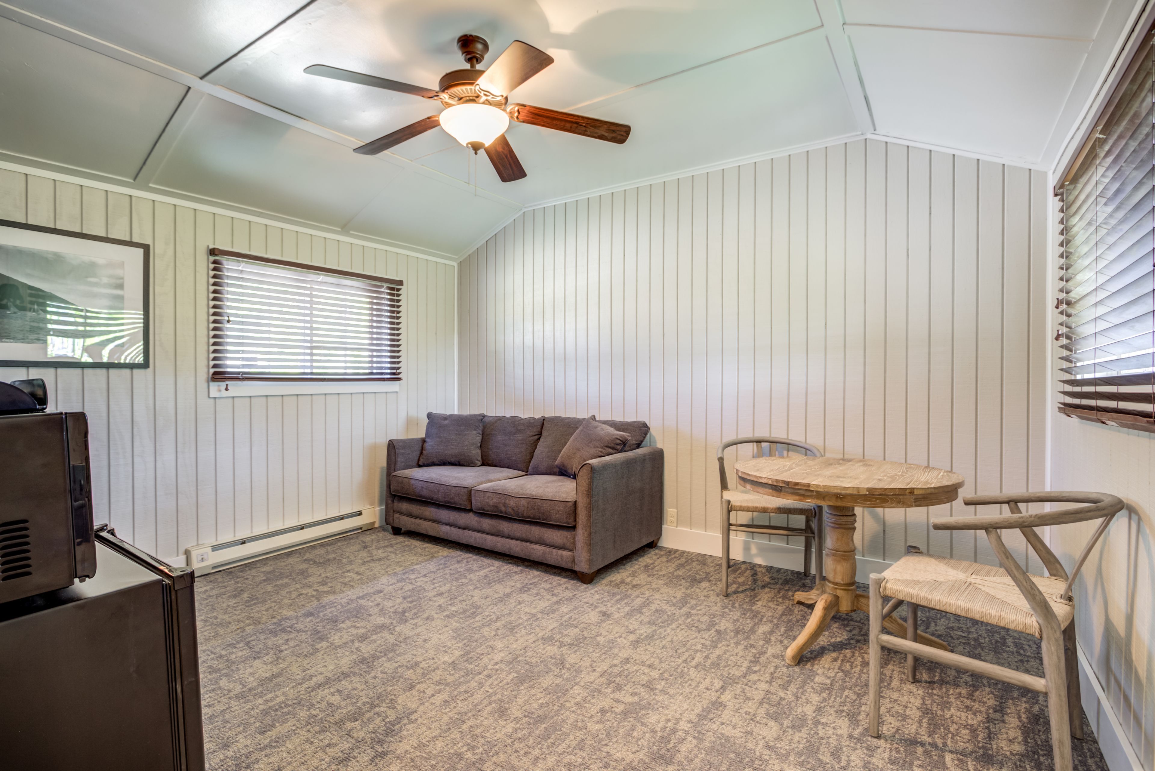 A room with a ceiling fan, a sofa, a round table, and a chair.