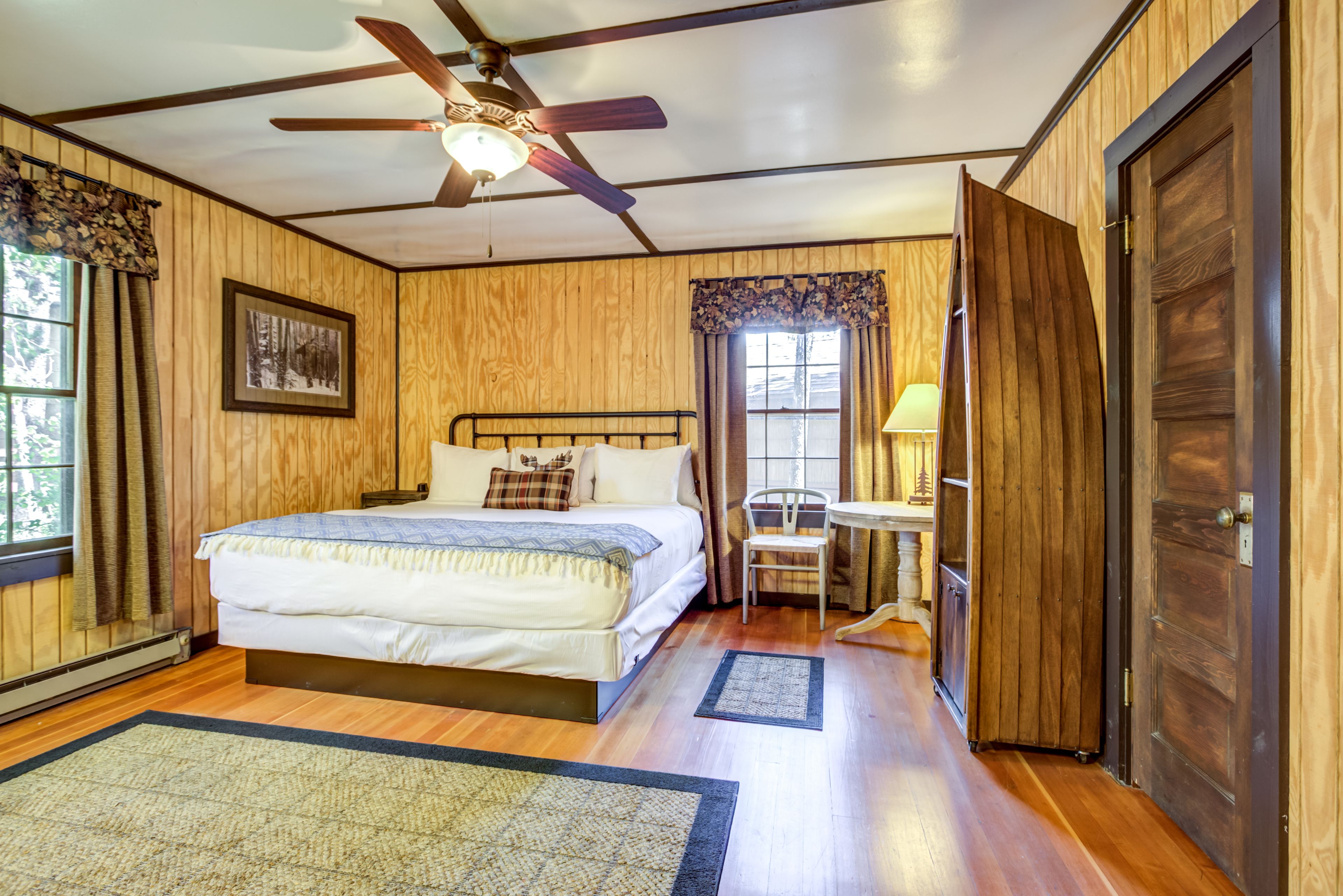 A bedroom with a bed, a ceiling fan, a window with curtains, a chair, and a door.