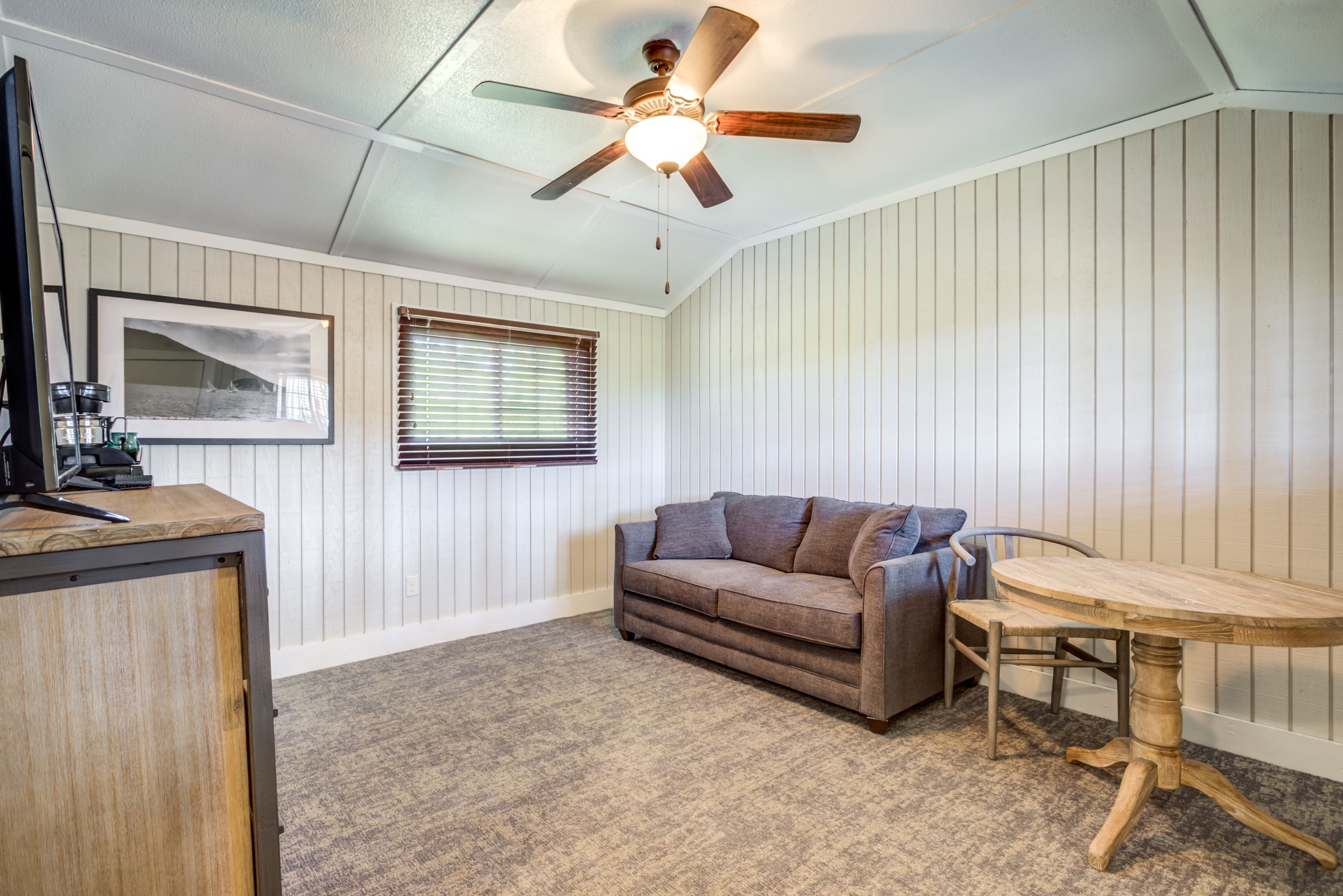 A room with a ceiling fan, a wooden table, a sofa, and a framed picture on the wall.