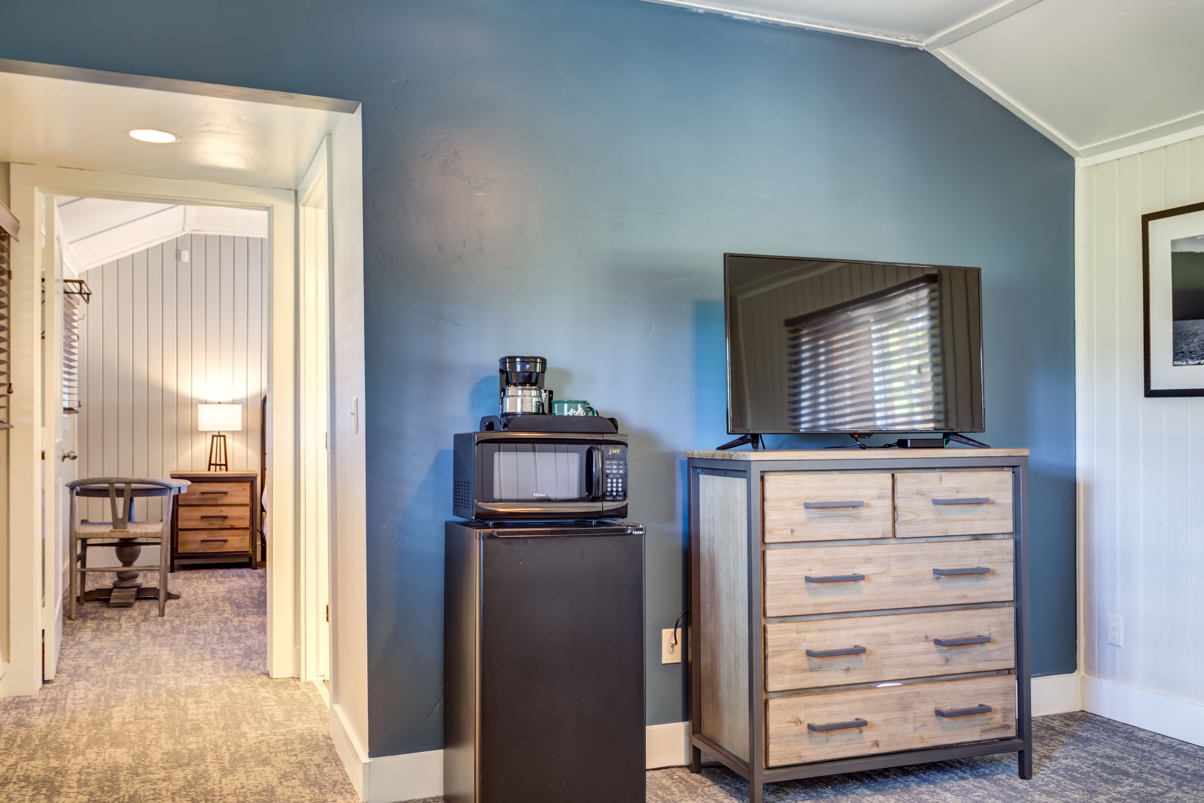 A compact room with a kitchenette, a wooden cabinet with drawers, a microwave, and a small refrigerator.