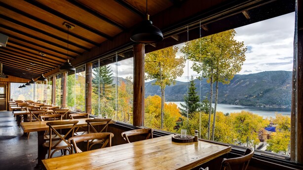 A restaurant with wooden tables and chairs, large windows offering a view of autumn foliage and mountains. - Grand Lake Lodge (Grand Lake)