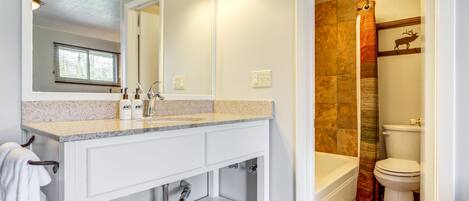 A bathroom with a white vanity, a large mirror, a bathtub, and a toilet.