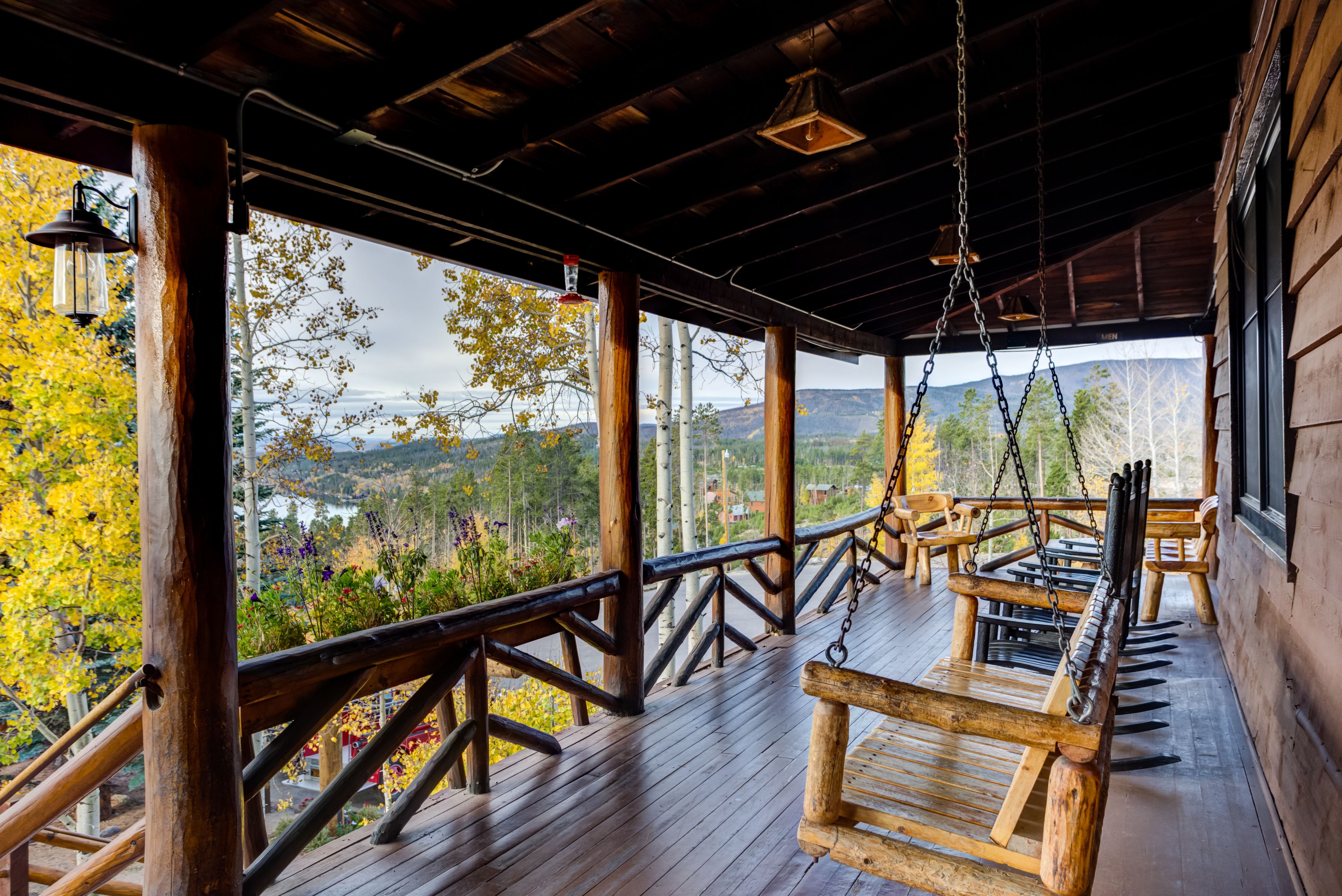 A wooden deck with a swing chair, wooden railings, and a view of a mountainous landscape.