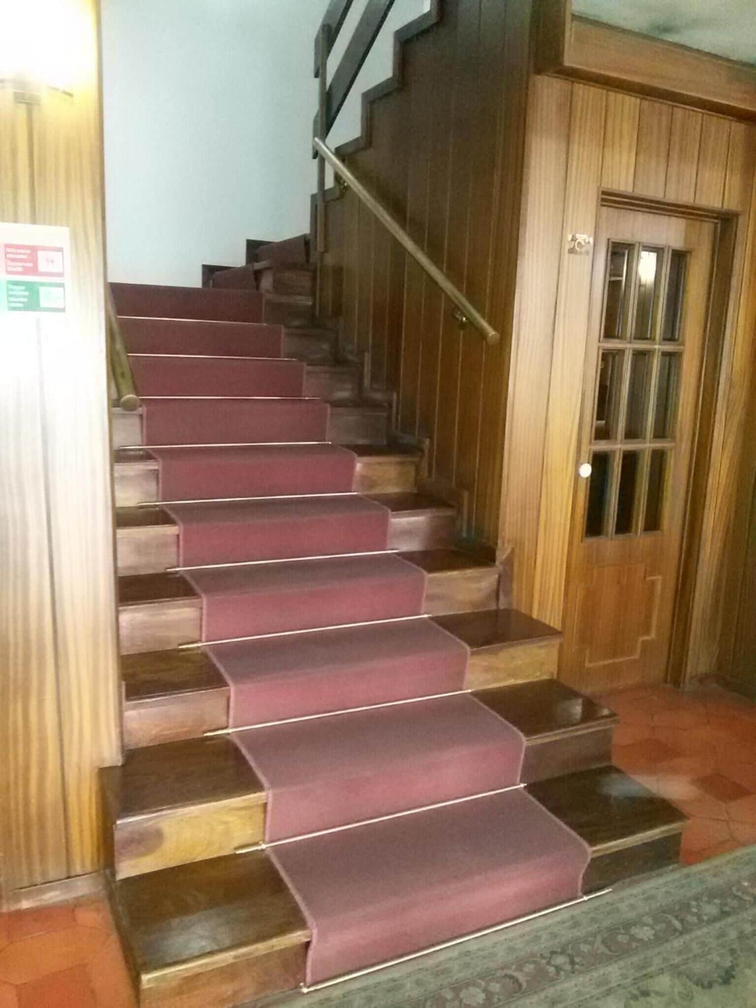 Una escalera con escalones de madera y una alfombra roja.