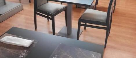 A hotel room with a dining area featuring tables and chairs, a wooden floor, and curtains.