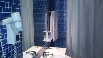 Een badkamer met blauwe betegelde wanden, een witte wastafel, een spiegel, een haardroger en een douchegordijn.