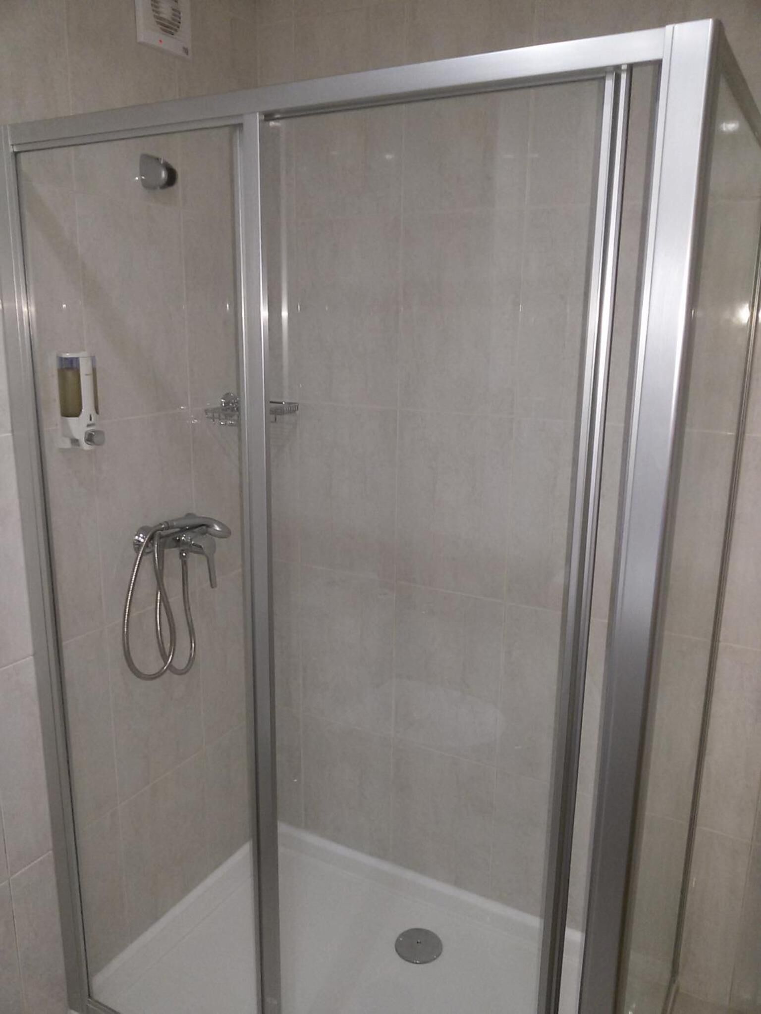 Cabina de ducha con paredes de vidrio, cabezal de ducha de mano y grifo empotrado.
