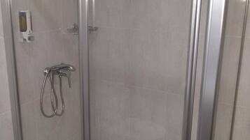 Cabina de ducha con paredes de vidrio, cabezal de ducha de mano y grifo empotrado.