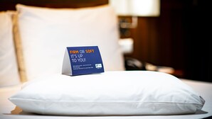 A bed with a pillow and a sign indicating firmness options.