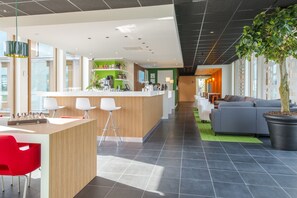 A modern hotel lobby with a reception desk, bar area, seating, and a large potted tree. - Holiday Inn Express Utrecht - Papendorp by IHG (Utrecht)