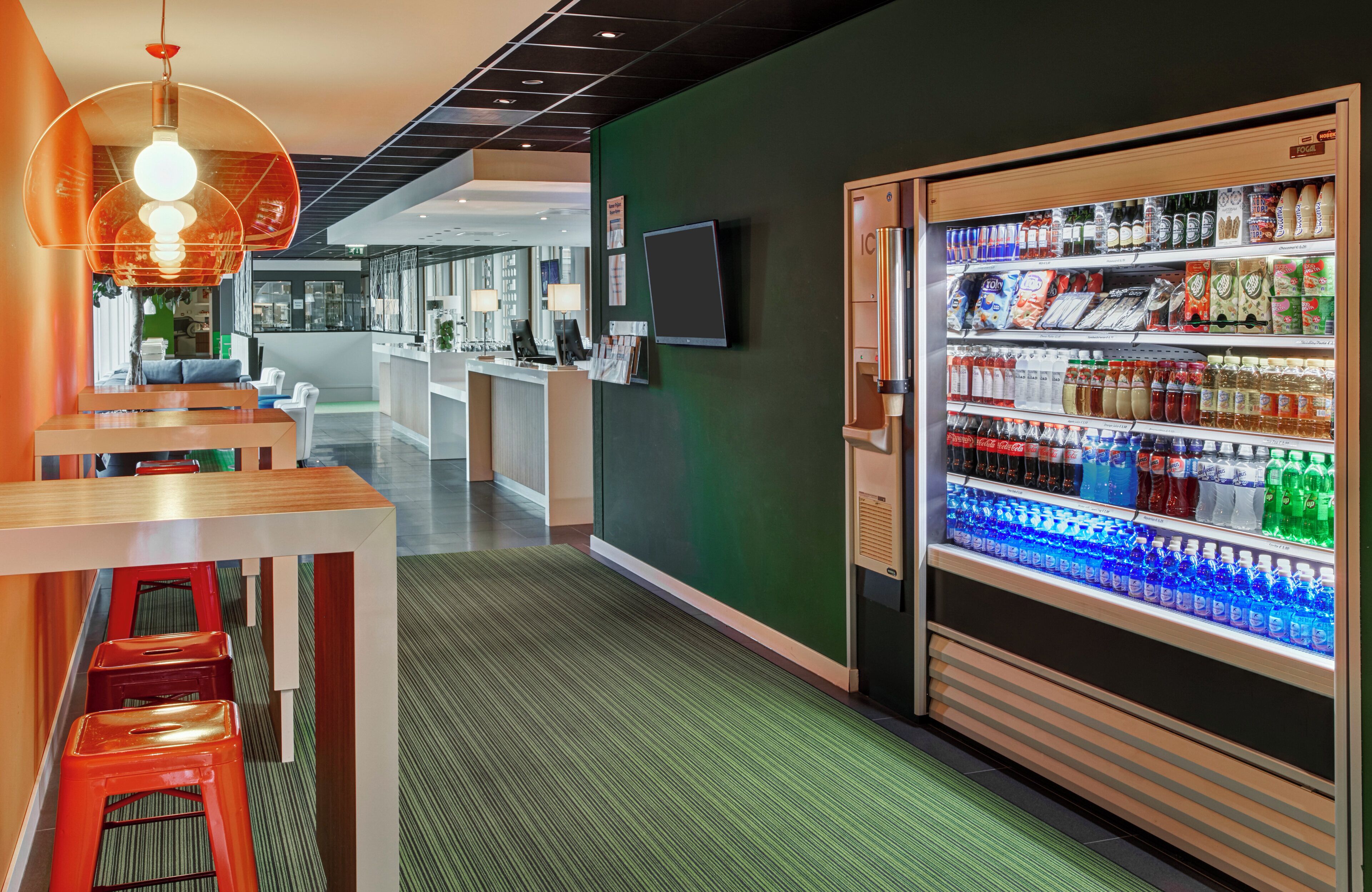Un moderno vestíbulo de hotel con mostrador de recepción, zona de estar y máquina expendedora de bebidas.