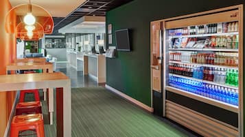 Un moderno vestíbulo de hotel con mostrador de recepción, zona de estar y máquina expendedora de bebidas.