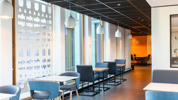 A modern restaurant with a long counter, blue chairs, and pendant lighting.