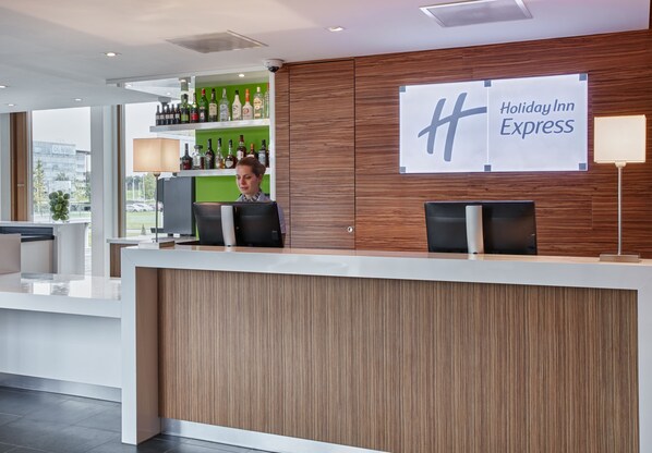A Holiday Inn Express reception desk with a wooden panel design, a bar area with liquor bottles, and a large sign with the hotel name. - Holiday Inn Express Utrecht - Papendorp by IHG (Utrecht)