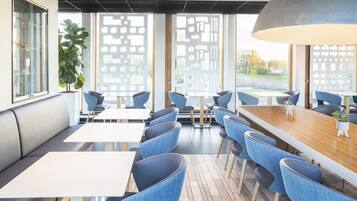 A modern dining area with a long wooden table, blue upholstered chairs, and a large potted plant.