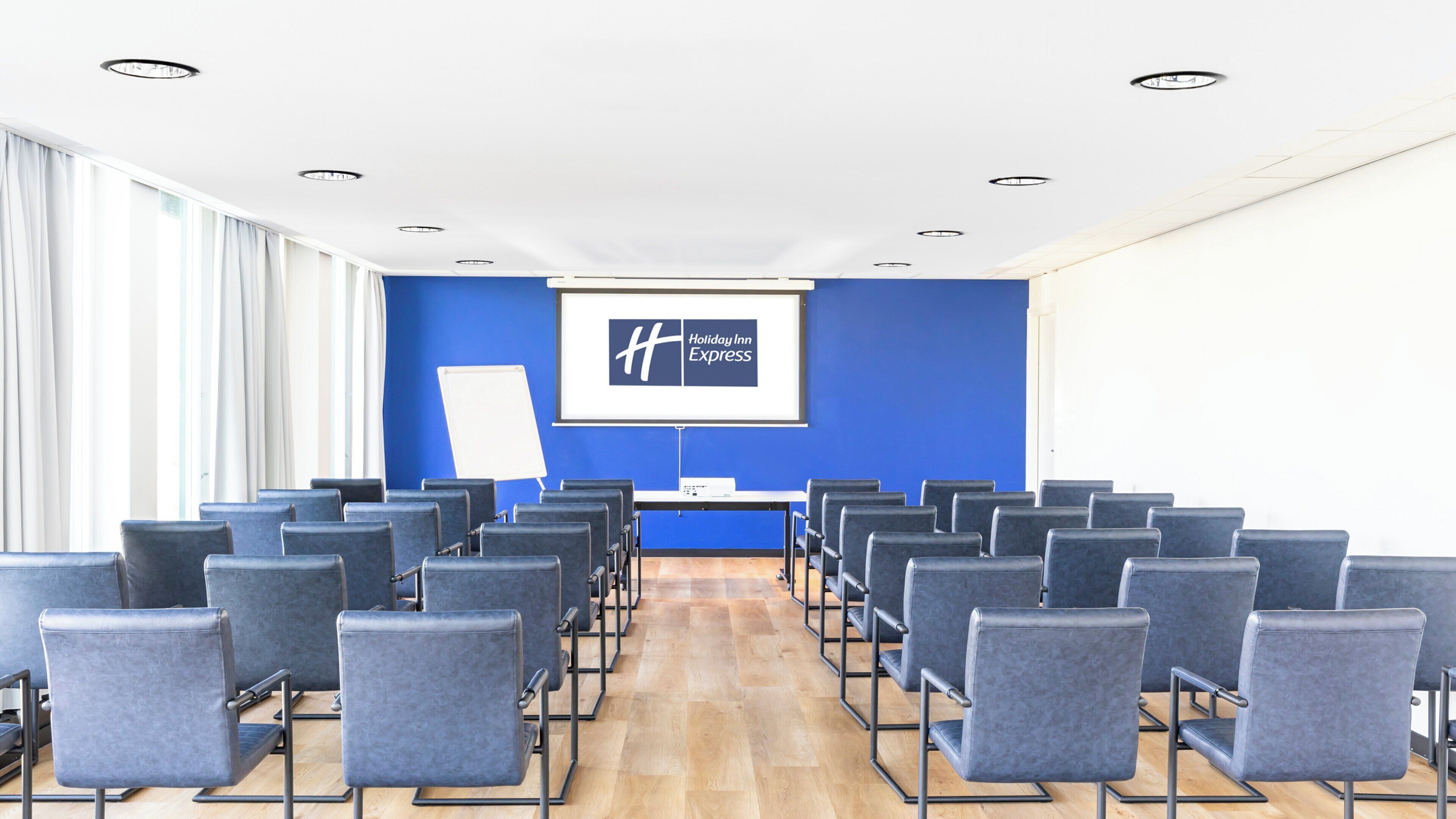 A conference room with rows of chairs, a projector screen, and a whiteboard.
