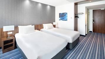 A hotel room with two beds, a nightstand with a lamp, a painting on the wall, and a door leading to another room.