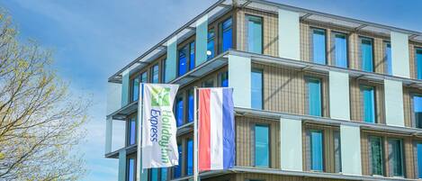 Un immeuble à plusieurs étages doté d’une architecture moderne, caractérisé par de grandes fenêtres et un balcon aux étages supérieurs.