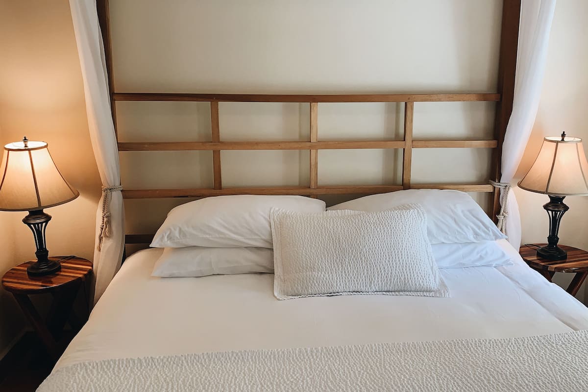 A neatly made bed with white linens and pillows, flanked by two bedside lamps on wooden nightstands.