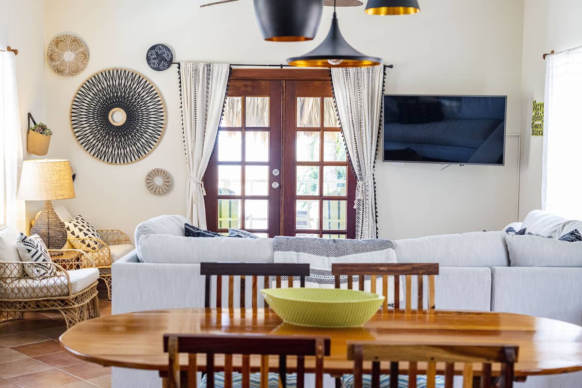 A living room with a sofa, a dining table with chairs, a TV mounted on the wall, and decorative wall art.