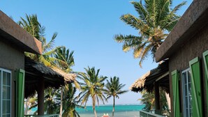 A view from a balcony overlooking a beach with palm trees, a pool, and a thatched-roof building. - Caye Casa (San Pedro)