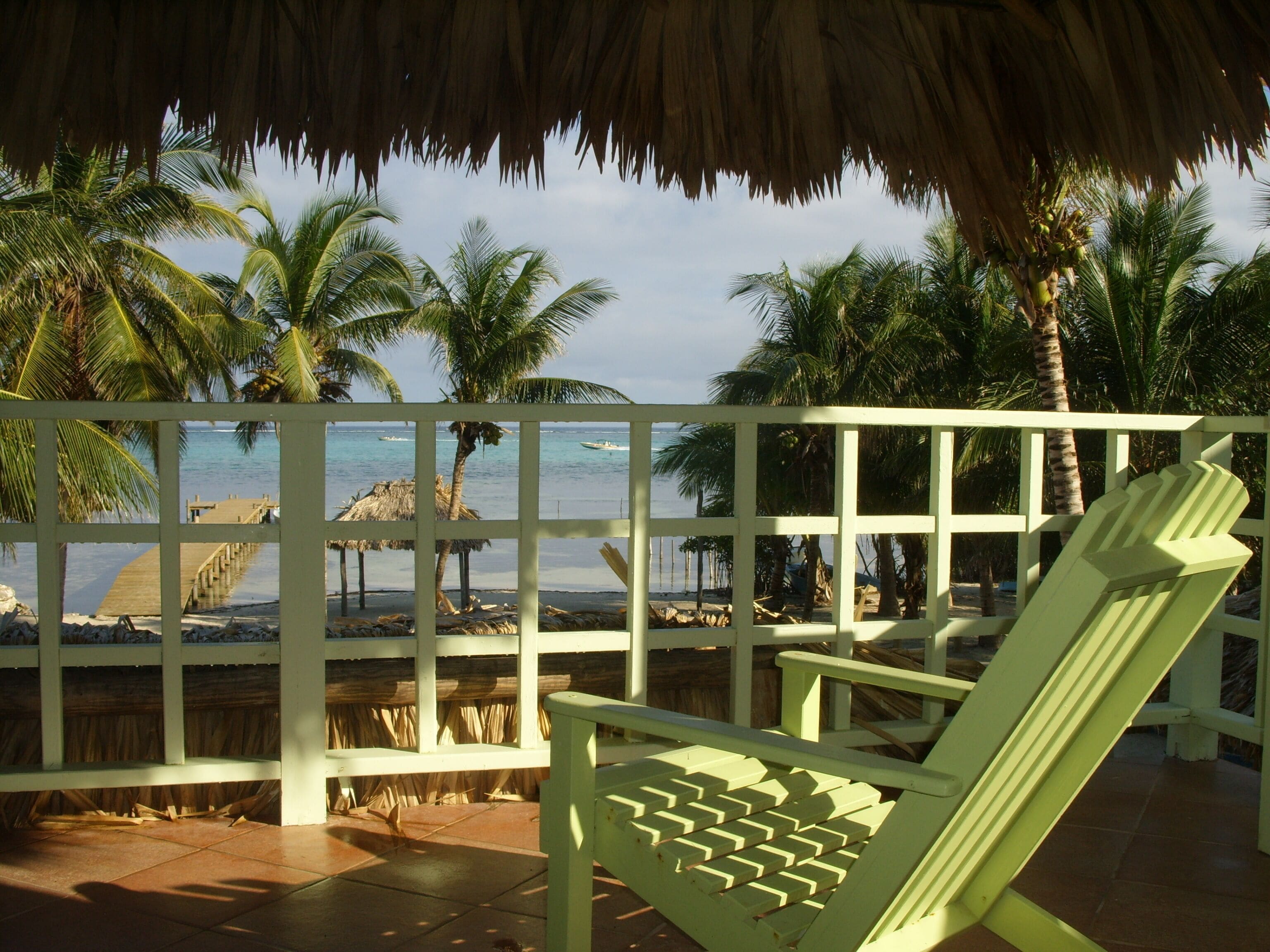 A beach view with a wooden deck, palm trees, and a thatched roof structure.