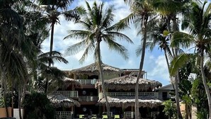 A beachfront hotel with thatched roofs, clear shallow waters, and palm trees. - Caye Casa (San Pedro)