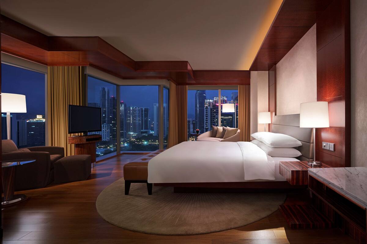 Een moderne hotelkamer met een groot bed, een televisie en uitzicht op de skyline van de stad 's nachts.
