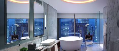 A modern bathroom with a large bathtub, a vanity with a mirror, and a city view through large windows.