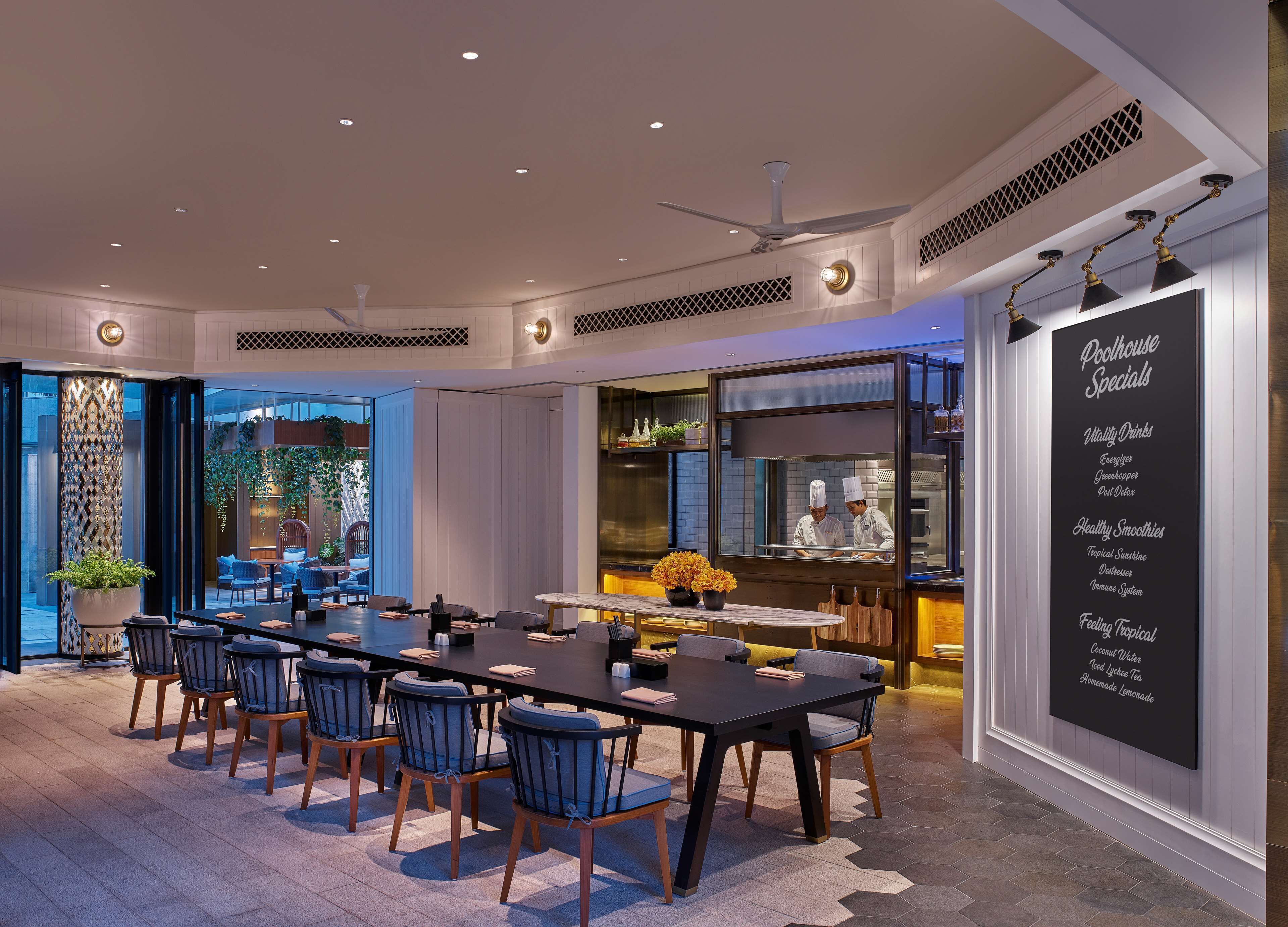 A modern dining area with a long table, chairs, and a view of the kitchen.