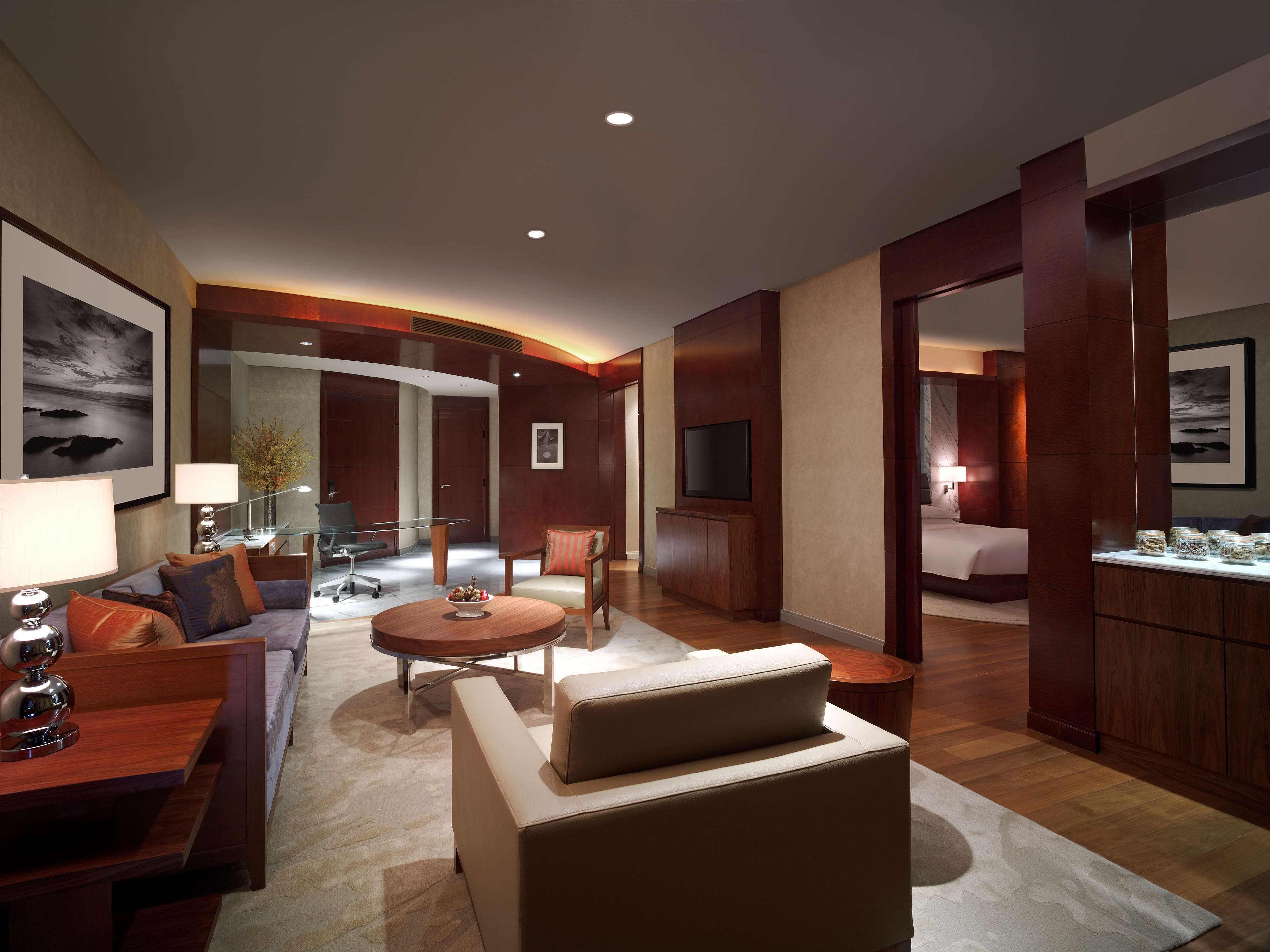 A modern hotel room with a living area, a separate bedroom, a dining area, and a bathroom.