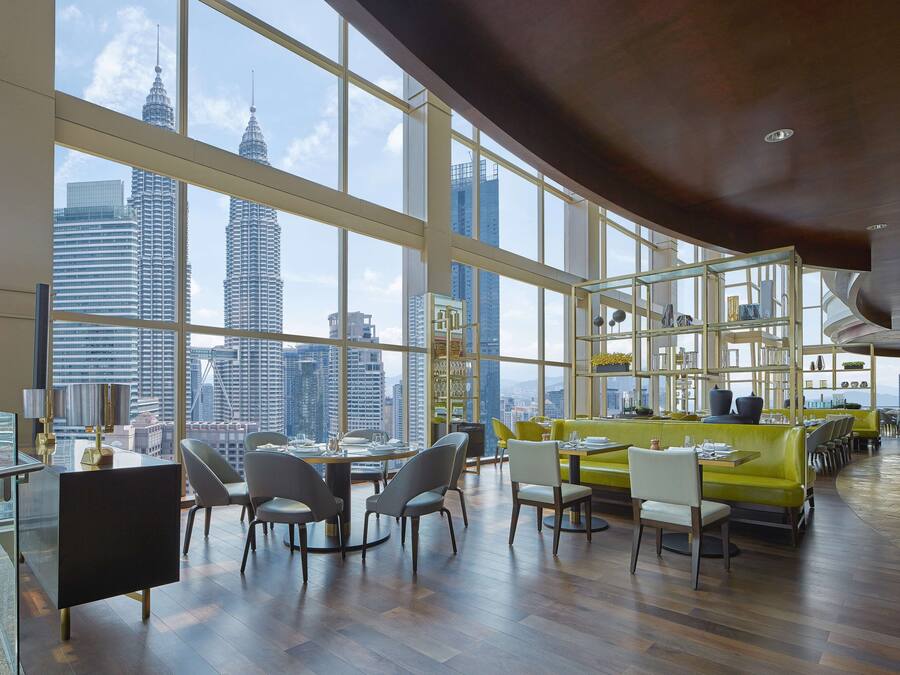 Un comedor moderno con techos altos y ventanas amplias que ofrecen vistas de la ciudad, incluyendo las Torres Petronas.