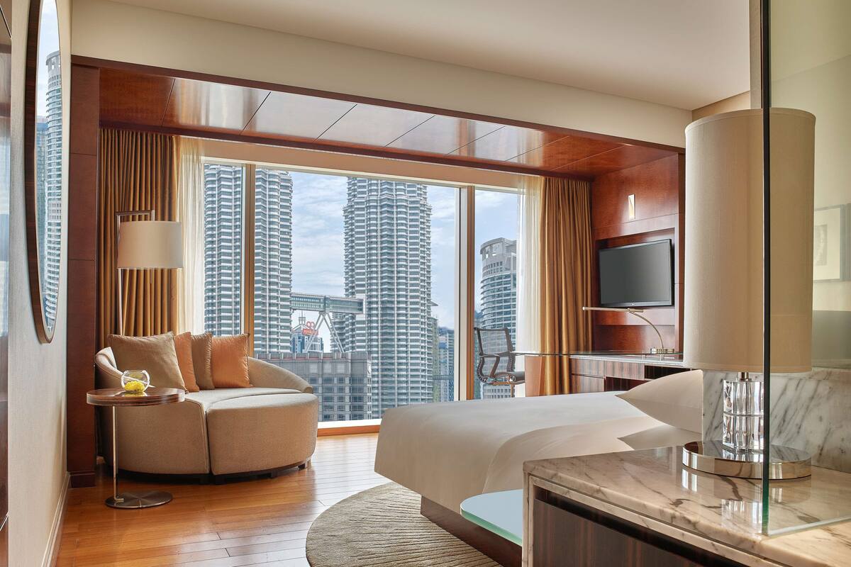 Een moderne hotelkamer met een groot bed, een bank, een televisie en uitzicht op hoge gebouwen.