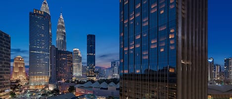 A cityscape at dusk with modern high-rise buildings, including a distinctive skyscraper with a pointed top.