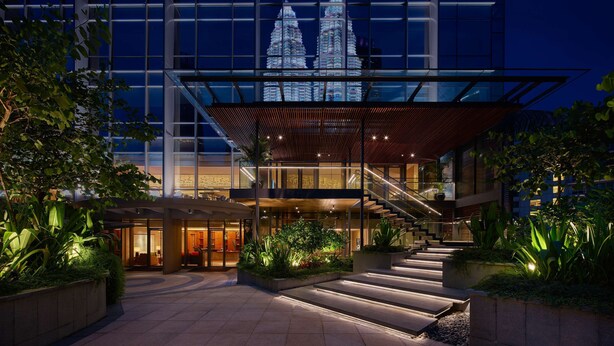 A modern building with a glass facade, a staircase leading to the entrance, and a view of the Petronas Towers in the background.