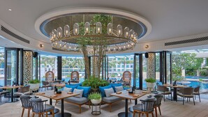 A modern indoor dining area with round tables, comfortable seating, and a central decorative light fixture.