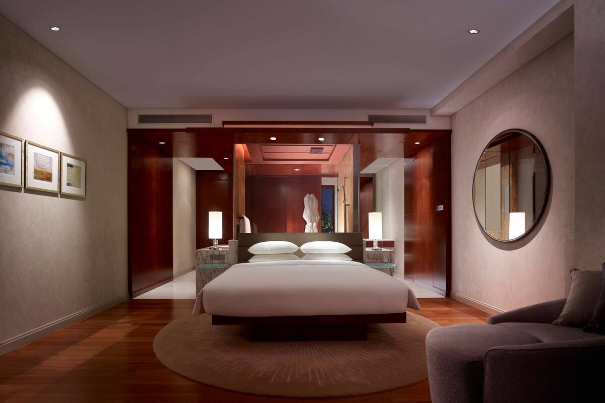 Een moderne slaapkamer met een groot bed, een ronde spiegel en kunstwerken aan de muur.