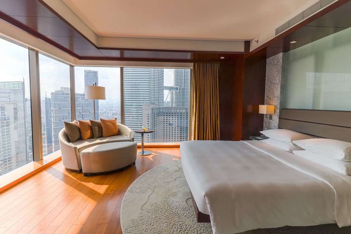 Een moderne hotelkamer met een groot bed, een bank en uitzicht op de skyline door middel van kamerhoge ramen.