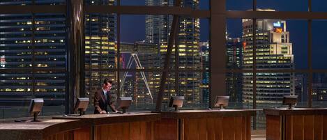 A modern reception area with a curved desk, large windows offering a cityscape view, and a digital clock displaying 7:42.