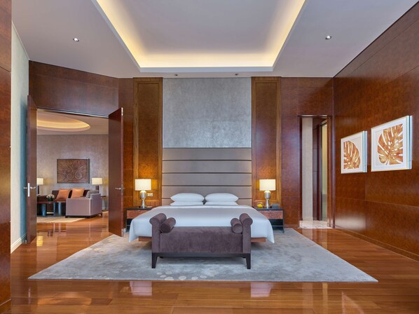 Quarto de hotel moderno com uma cama grande, duas mesas de cabeceira com luminárias, um banco e uma grande obra de arte na parede.