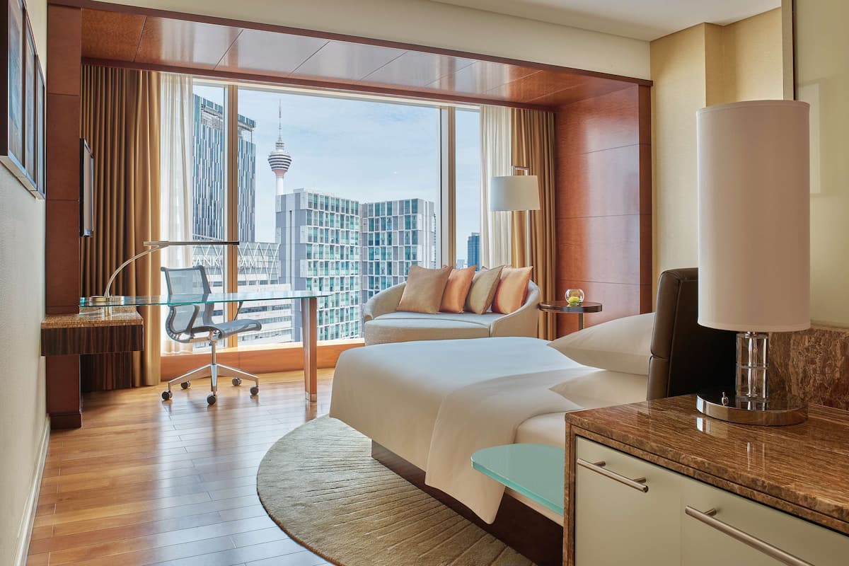 Een hotelkamer met een groot bed, een bureau met stoel, een lamp en uitzicht op een stadsbeeld.