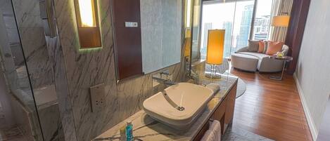 A modern bathroom with a marble sink, a glass shower enclosure, and a city view through large windows.