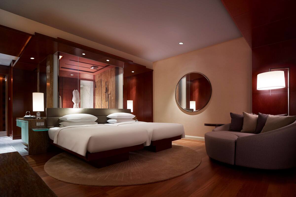 Een moderne hotelkamer met een groot bed, een slaapbank, een ronde spiegel en een nachtkastje.