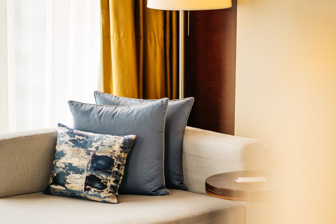 A sofa with two pillows, a small round table, and a lamp.