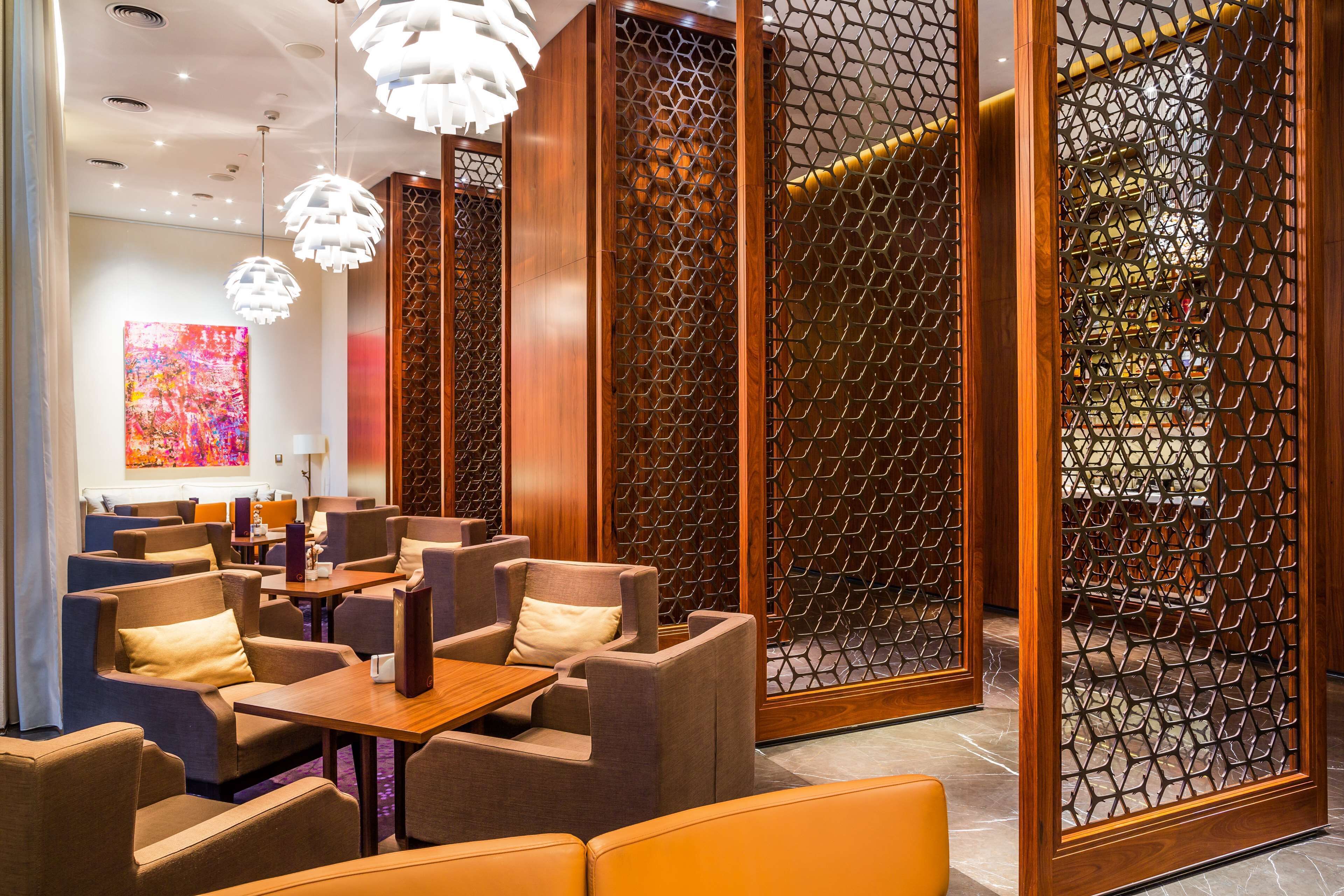 A modern hotel lobby with seating areas, decorative lighting, and a large abstract painting on the wall.